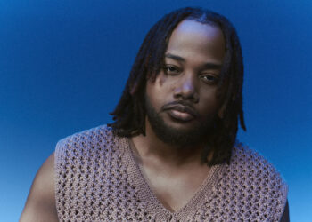 A photo of singer, songwriter and producer Leon Thomas against a blue backdrop.