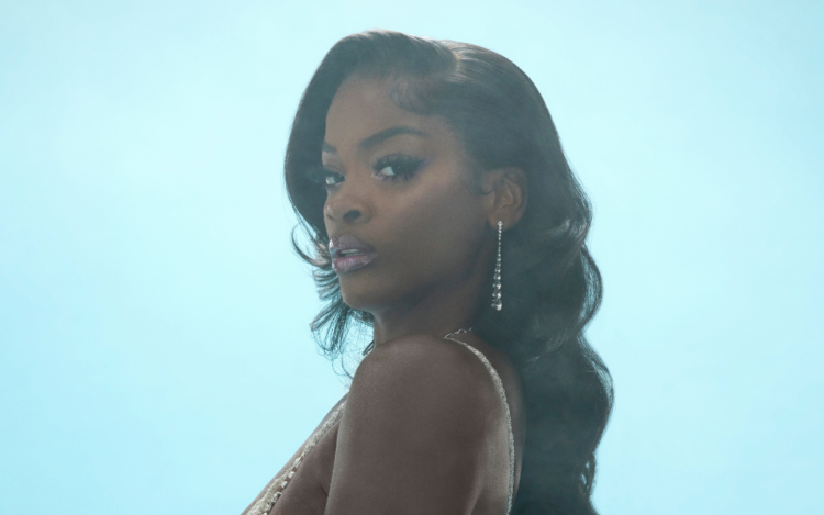 A photo of R&B singer Ari Lennox in front of a sky blue backdrop