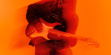 A photo of singer Leon Thomas holding an electric guitar against an orange backdrop