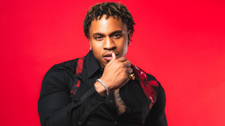 A photo of R&B singer and actor Rotimi in front of a red backdrop